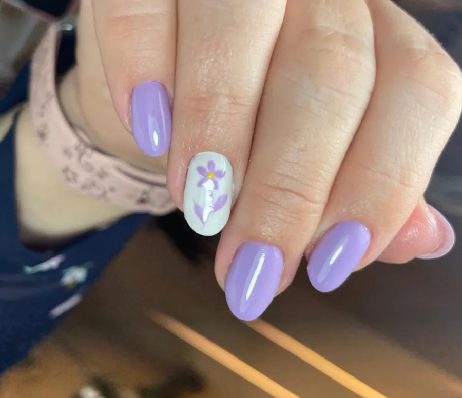 Manicura semipermanente en tono lila con uña decorada con una flor pintada a mano